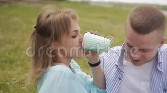 在河边约会的情侣一个女孩在纸杯里喝咖啡抚摸一只小狗视频的预览图