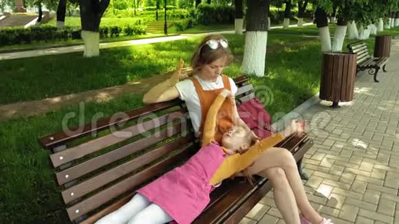 妈妈带着女儿学龄前女孩躺在公园里一个年轻女人的腿上的长凳上夏日晴天视频的预览图