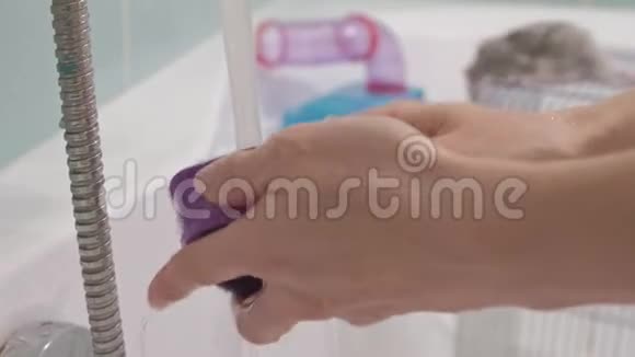一个年轻的女人照顾一只宠物用水清洗水龙头下的食物碗打扫浴室里的笼子一个视频的预览图