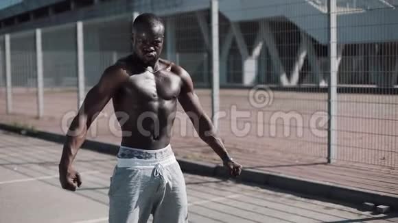 运动的非裔美国男人裸露的躯干摆姿势显示他的肌肉在户外在体育场附近摆姿势的黑人视频的预览图
