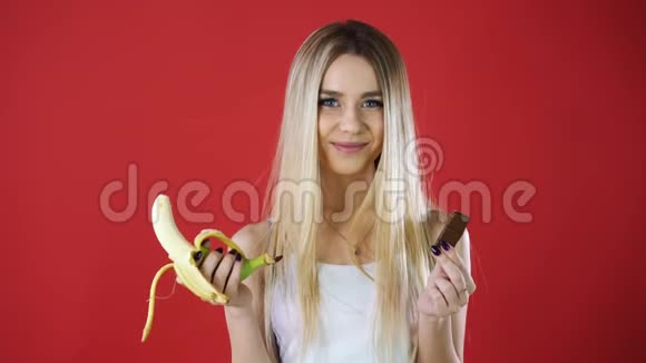 看有巧克力和香蕉的女人试图做出健康的选择控制她的体重隔离在红墙上视频的预览图
