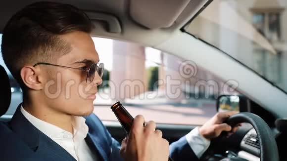 年轻的商人在车里喝啤酒坏消息由于坏交易或坏消息而心情不好的人喝醉了开车视频的预览图