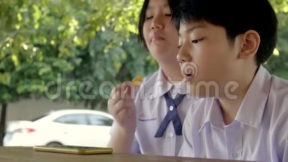 慢动作4K的快乐亚洲儿童穿着校服享受吃薯片的微笑视频的预览图