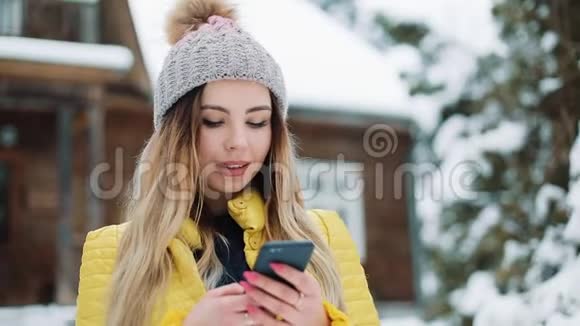 快乐的年轻女孩使用智能手机上的应用程序微笑和手机短信穿冬衣的女人视频的预览图