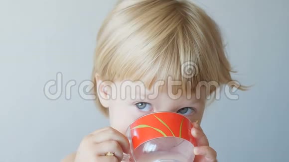 一个金发小女孩在家喝红杯子里的牛奶视频的预览图