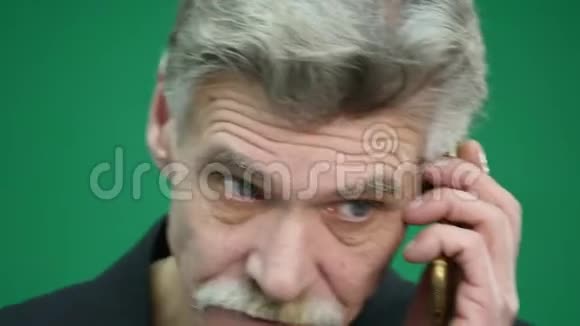 愤怒的老人在绿色背景下用手机说话视频的预览图