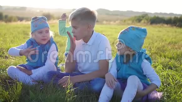 孩子们坐在公园的草坪上笑拥抱做空气亲吻孩子们露天度假视频的预览图