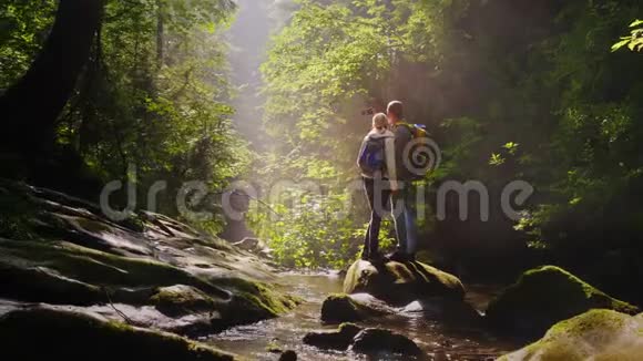 一对旅行者被拍到在一个风景如画的地方在一条山河附近的森林里视频的预览图
