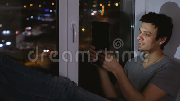 男人在平板电脑上聊天笑着夜深人静的坐在窗台上视频的预览图