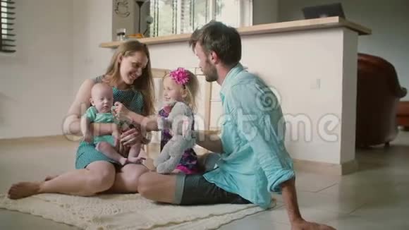美丽的年轻家庭妈妈爸爸小女儿和小儿子坐在厨房的地板上慢动作视频的预览图