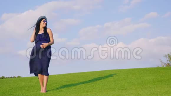 期待孩子的时髦女人站在绿色的草地上风吹着她的长发视频的预览图