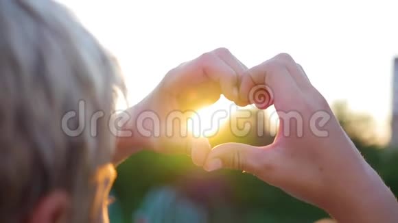 在太阳下用手做心脏的人剪影手中的心形与里面的夕阳视频的预览图