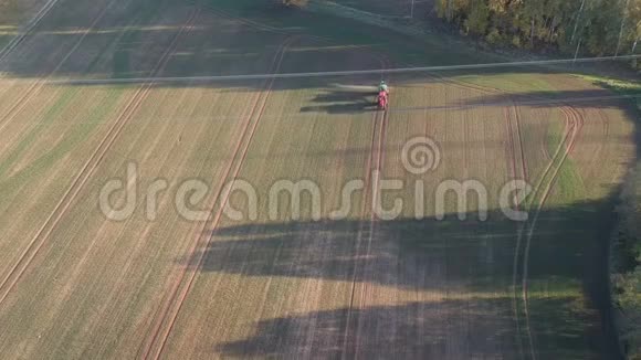 傍晚农业拖拉机喷洒秋时作物田芽空中视频的预览图