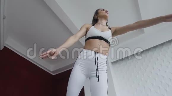 穿白色运动服的健身女孩单腿站立室内瑜伽练习背景宽敞白色和红色墙壁视频的预览图