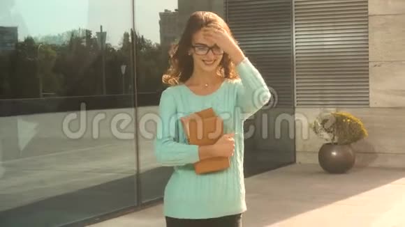 年轻可爱的黑发女孩戴着眼镜走在街上手里拿着书视频的预览图