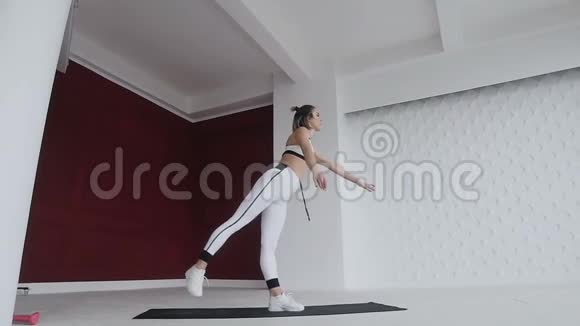 穿白色运动服的女人站在一条腿上瑜伽练习在室内背景宽敞的白色和红色墙壁上Yogi视频的预览图