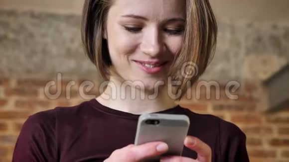 年轻漂亮的女孩正在她的智能手机上输入信息微笑交流理念砖背景视频的预览图
