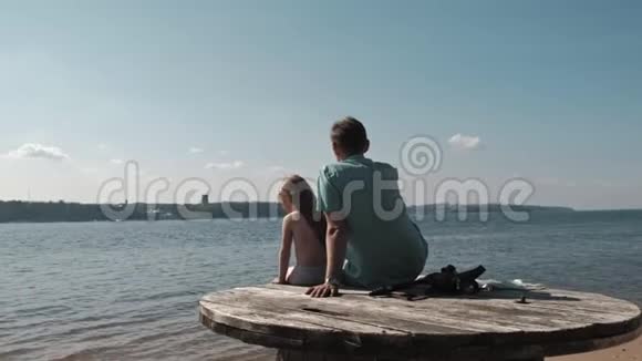 父亲和小女儿正坐在河岸海滩上的一个木台阶上视频的预览图