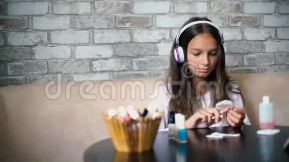 可爱的女孩戴着耳机和家里的衣服在电话里聊天做指甲剪指甲视频的预览图