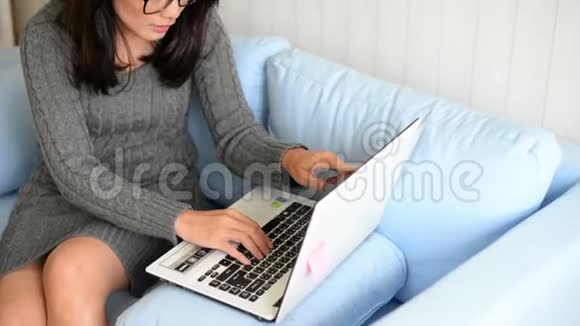 亚洲女人坐在沙发上在家里用笔记本电脑视频的预览图