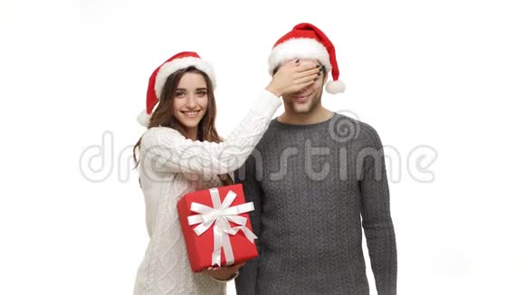 年轻的女朋友闭上男朋友的眼睛给她的男朋友一个惊喜给她送了一份红色的圣诞礼物视频的预览图