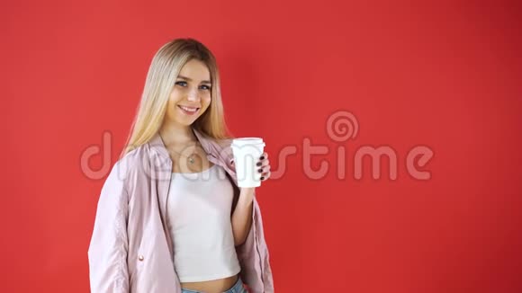 微笑放松的年轻女子和玻璃站着喝着咖啡拿起红墙背景视频的预览图