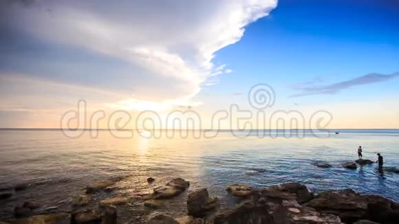 有鱼竿的人站在日落时的海石上视频的预览图