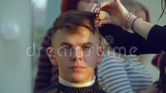 美容院理发店发型师给一个年轻的帅哥理发他坐在椅子上看着里面视频的预览图