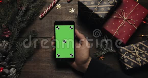 男性手拿着绿色屏幕的黑色智能手机另一只手把一些礼物盒放在桌子上铬键视频的预览图