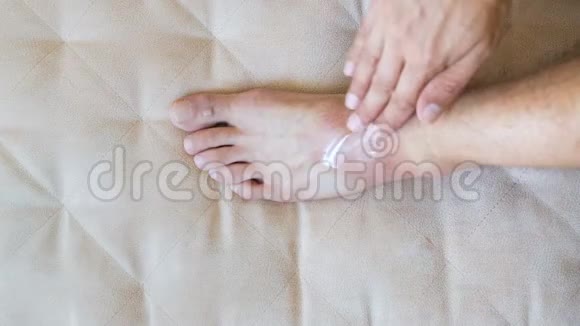 男人把白色的药膏霜擦在他受伤的脚踝上坐在家里的沙发上视频的预览图