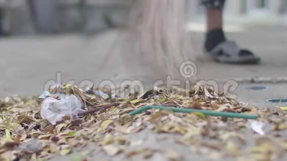 不明身份的女人在公园里用扫帚扫树叶特写视频的预览图