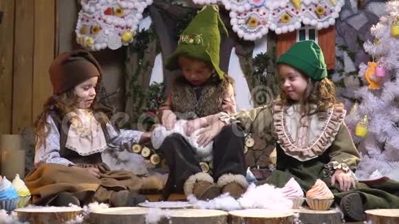 小妹妹和一个穿着旧圣诞衣服的金发男孩正坐在圣诞树旁旁边放着糖果和糖果视频的预览图