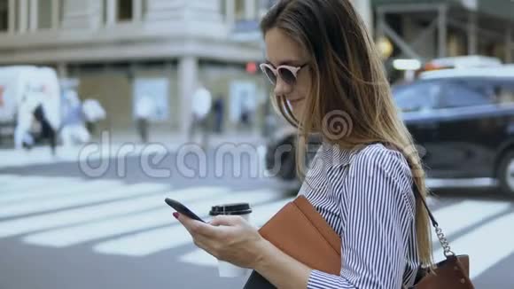 年轻漂亮的女商人拿着文件和咖啡杯忙碌的女性使用智能手机站在路边视频的预览图