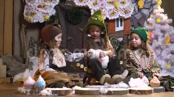 可爱的孩子们穿着古老的衣服坐在圣诞装饰中抚摸着毛茸茸的兔子慢动作视频的预览图