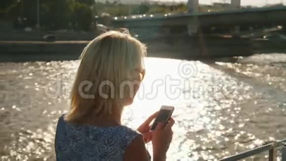 一个年轻的女人用智能手机在船上的河上航行在一片耀眼的背景下视频的预览图