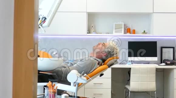 一个正在移动的滑块上的镜头显示一个年轻人坐在牙医椅上他看着镜头微笑视频的预览图