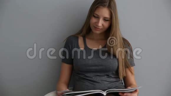 一个看起来像欧洲人的女孩在家在灰色的墙边喘着气看杂志视频的预览图