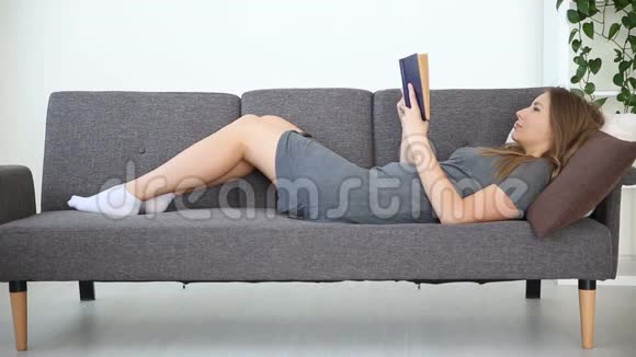 一个欧洲女孩在家里在客厅的灰色沙发上看书视频的预览图