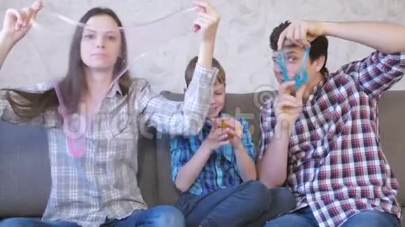 快乐的家庭妈妈儿子和爸爸玩泥浆坐在沙发上从黏液里看过去视频的预览图