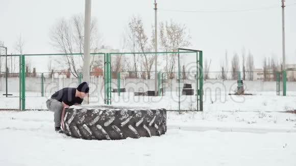 肌肉男在冬天举起一个大橡胶轮胎做交叉配合练习视频的预览图