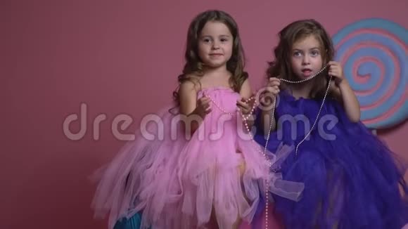 两个穿着粉色和蓝色连衣裙的女孩正坐在一颗大糖果的背景上动作缓慢视频的预览图