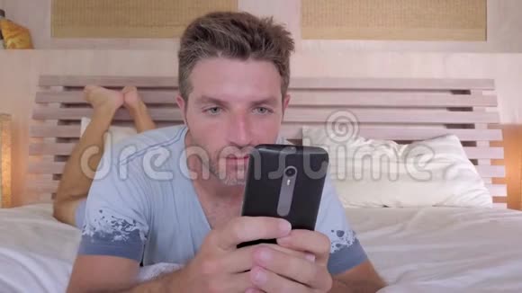 30岁或40岁无胡子的男人蓝眼睛躺在床上在手机上使用互联网社交媒体应用程序微笑着快乐地享受着早晨视频的预览图