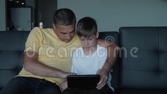 父子俩坐在沙发上看电影在平板电脑上玩游戏一个幸福的家庭视频的预览图