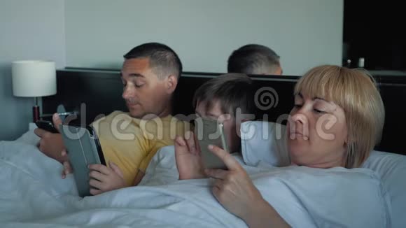 一个幸福的家庭一个孩子躺在床上使用数字平板电脑和智能手机现代技术视频的预览图