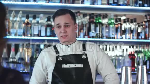 开朗的年轻酒吧老板微笑着和酒吧里的顾客交谈视频的预览图