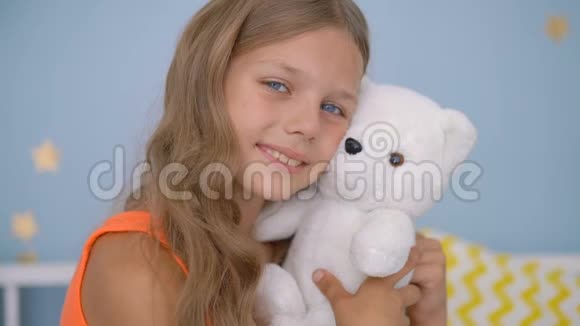 可爱的女孩抱着泰迪熊坐在家里的床上视频的预览图
