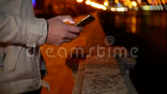 一名男子站在海滨在夜间灯光的背景下使用电话4k背景模糊视频的预览图