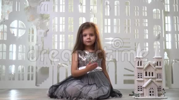 一个穿着灰色闪亮裙子的可爱女孩坐在玩具宫附近送上一个飞吻一张贺卡慢镜头拍摄视频的预览图