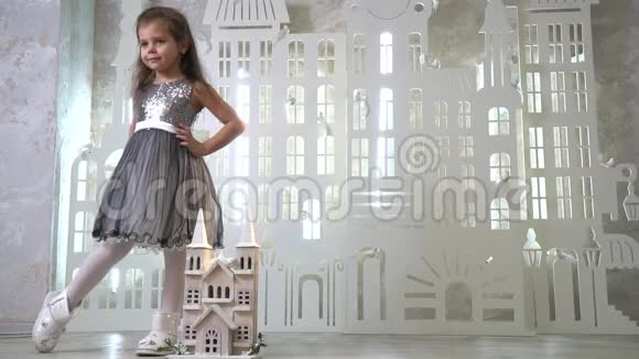 一个小女孩穿着闪亮的连衣裙穿着白色的鞋子在玩具城堡附近摆姿势动作缓慢视频的预览图