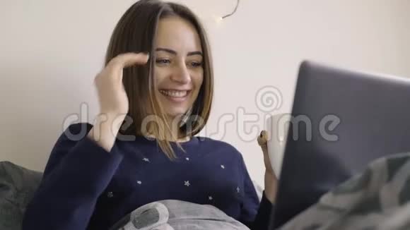 年轻女性在床上坐着时用笔记本电脑与朋友进行在线视频聊天视频的预览图